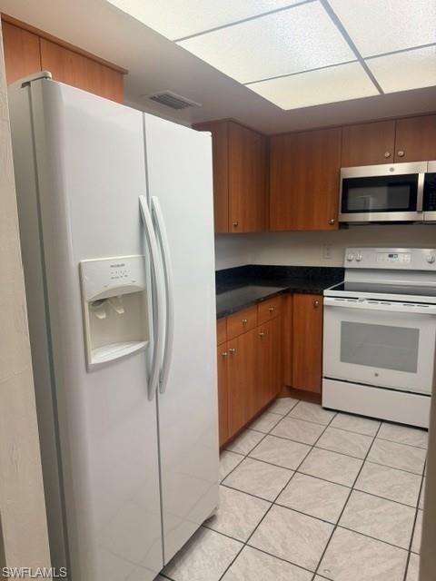 Kitchen featuring wood-finish cabinetry, black countertops, and a full suite of white appliances including a side-by-side refrigerator, electric range, and stainless steel microwave
