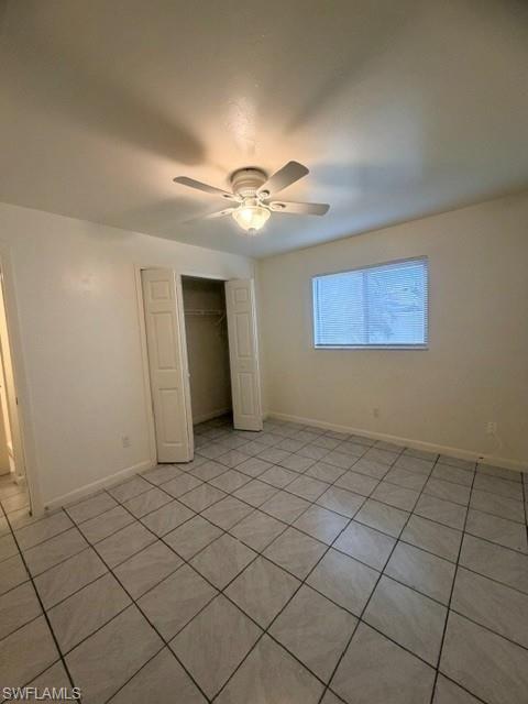 Spacious room with light-toned tiled flooring, a ceiling fan with integrated lighting, a window with horizontal blinds, and a double-door closet with shelving