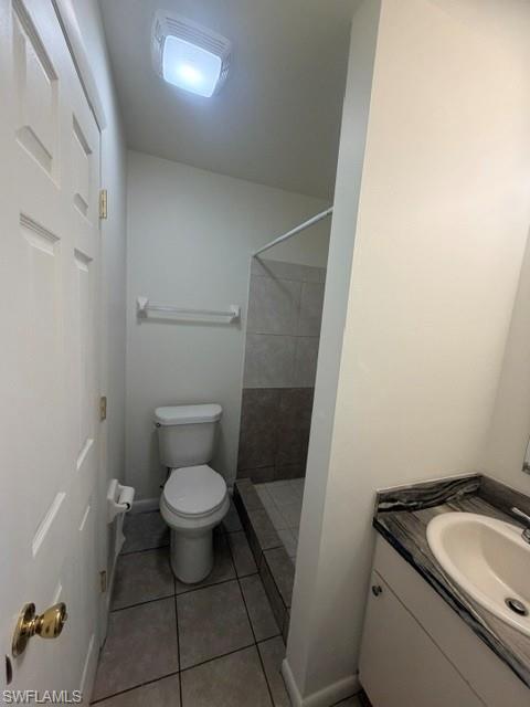Bathroom featuring a single vanity with an integrated sink and dark stone-look countertop, a standard toilet, and a tiled shower stall