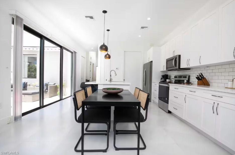 Open-concept kitchen and dining area featuring white cabinetry, subway tile backsplash, and stainless steel appliances