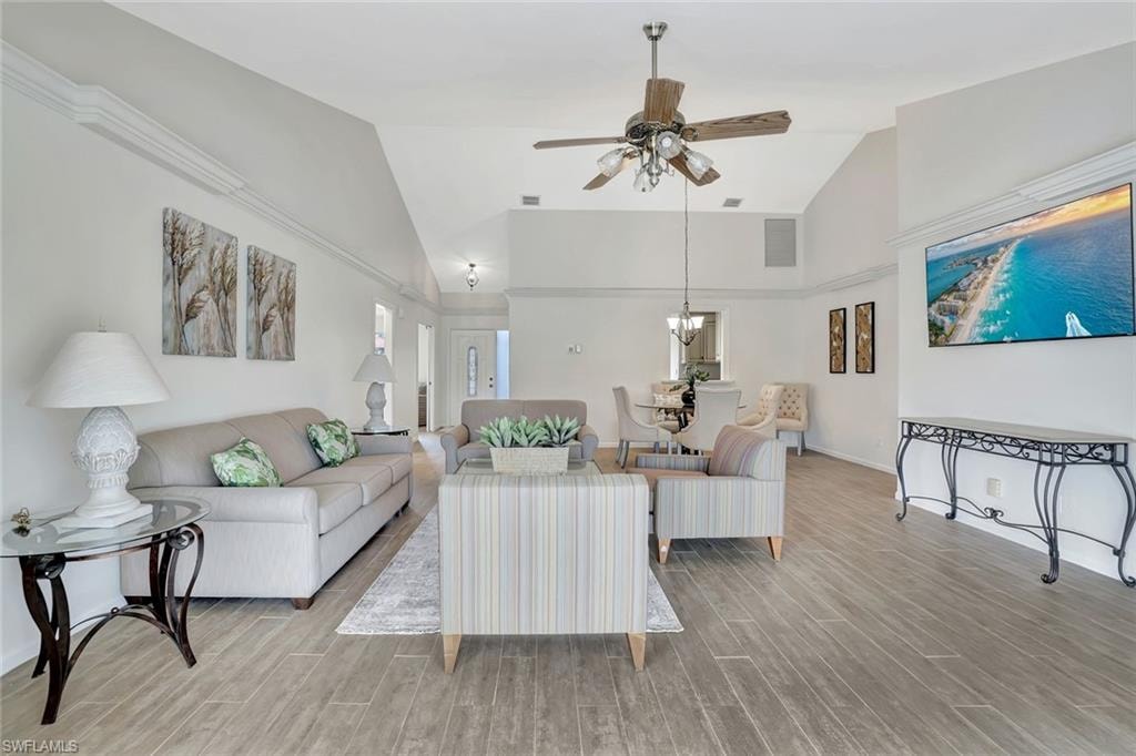 Living room featuring wood finished floors, ceiling fan, a chandelier, baseboards, and high vaulted ceiling