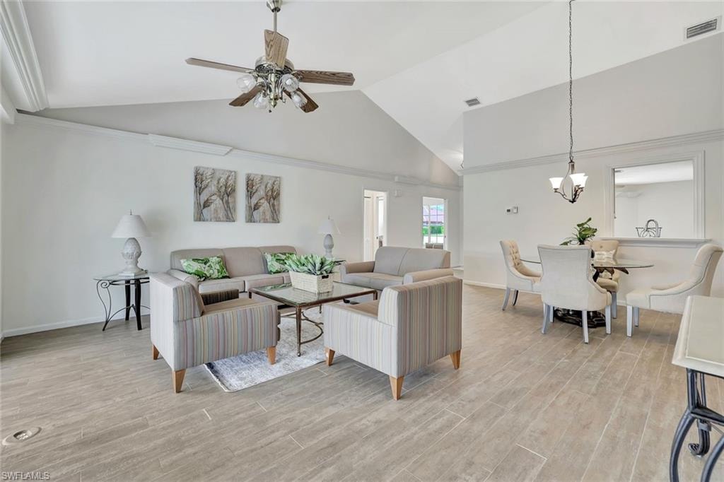 Living room with a chandelier, high vaulted ceiling, ceiling fan, light wood-style flooring, and baseboards