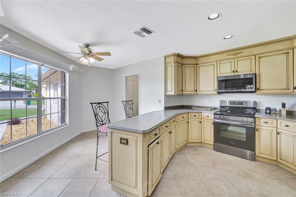 Kitchen with appliances with stainless steel finishes, cream cabinets, a ceiling fan, light tile patterned floors, and recessed lighting