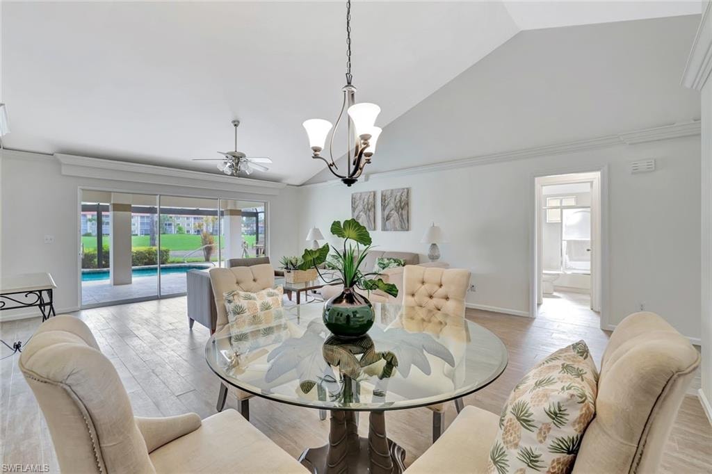 Dining space with vaulted ceiling, a chandelier, ceiling fan, light wood-type flooring, and crown molding