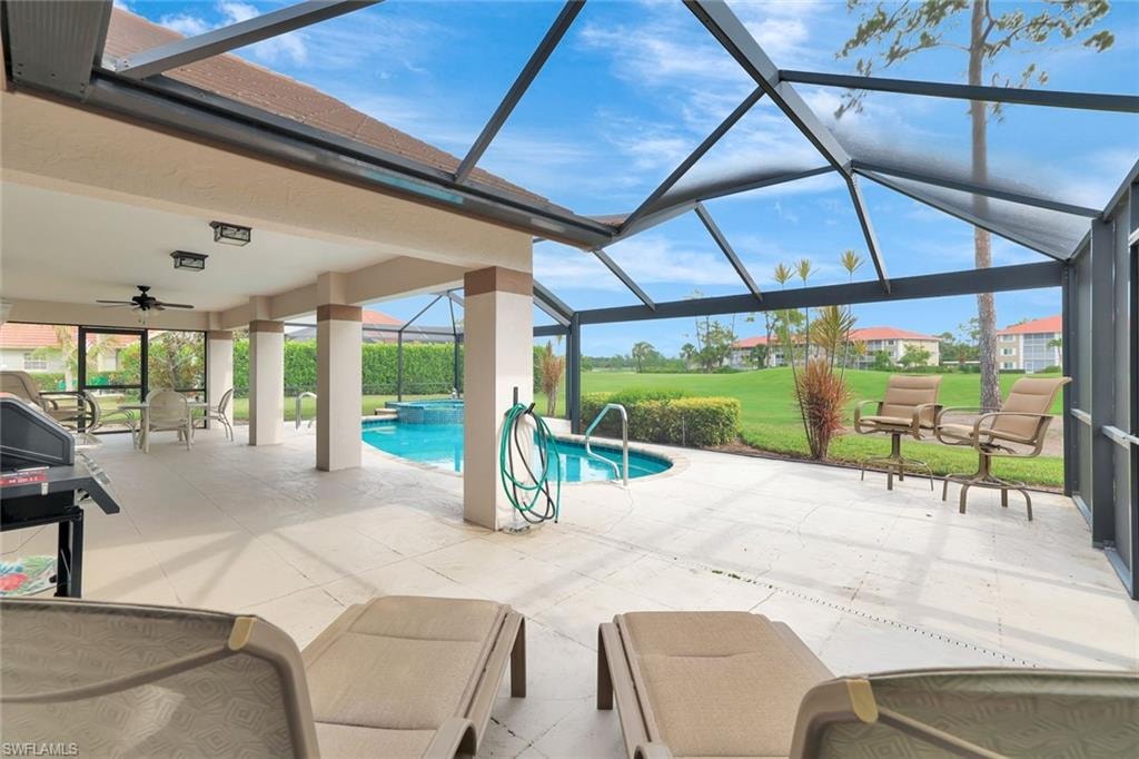 View of pool featuring a patio, glass enclosure, a ceiling fan, and a pool with connected hot tub