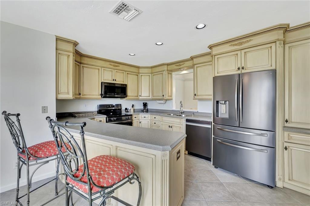 Kitchen featuring appliances with stainless steel finishes, cream cabinetry, recessed lighting, light tile patterned floors, and a sink