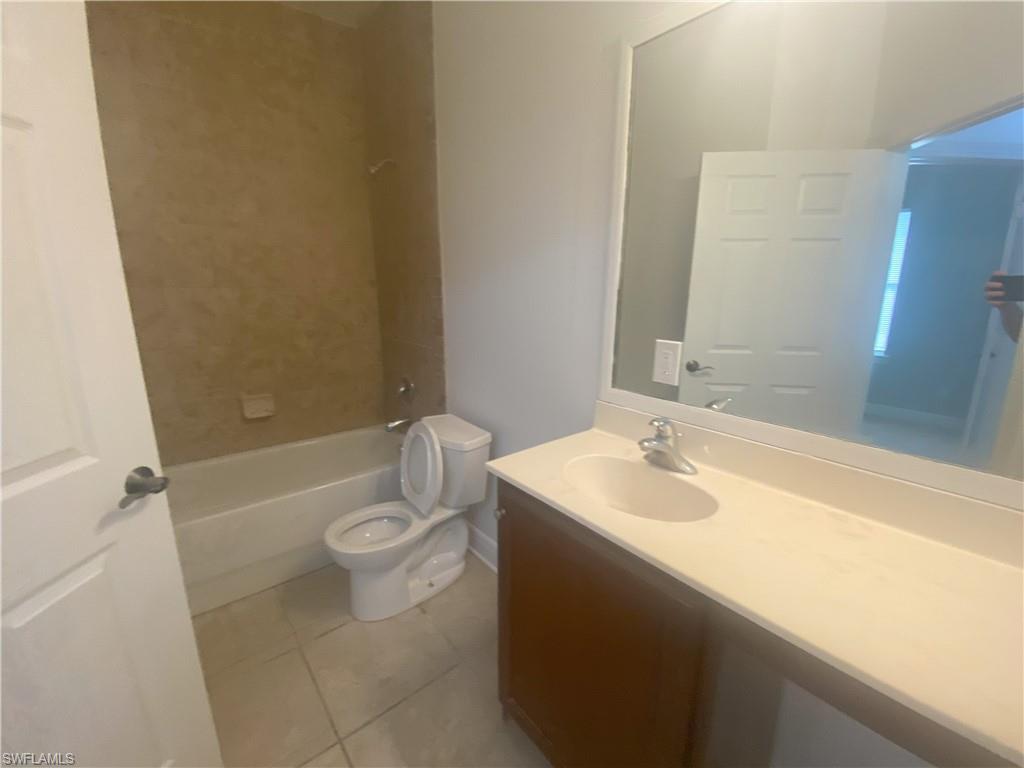 Bathroom featuring a vanity with an integrated sink and light-colored countertop, a framed mirror, and a bathtub with a tiled surround