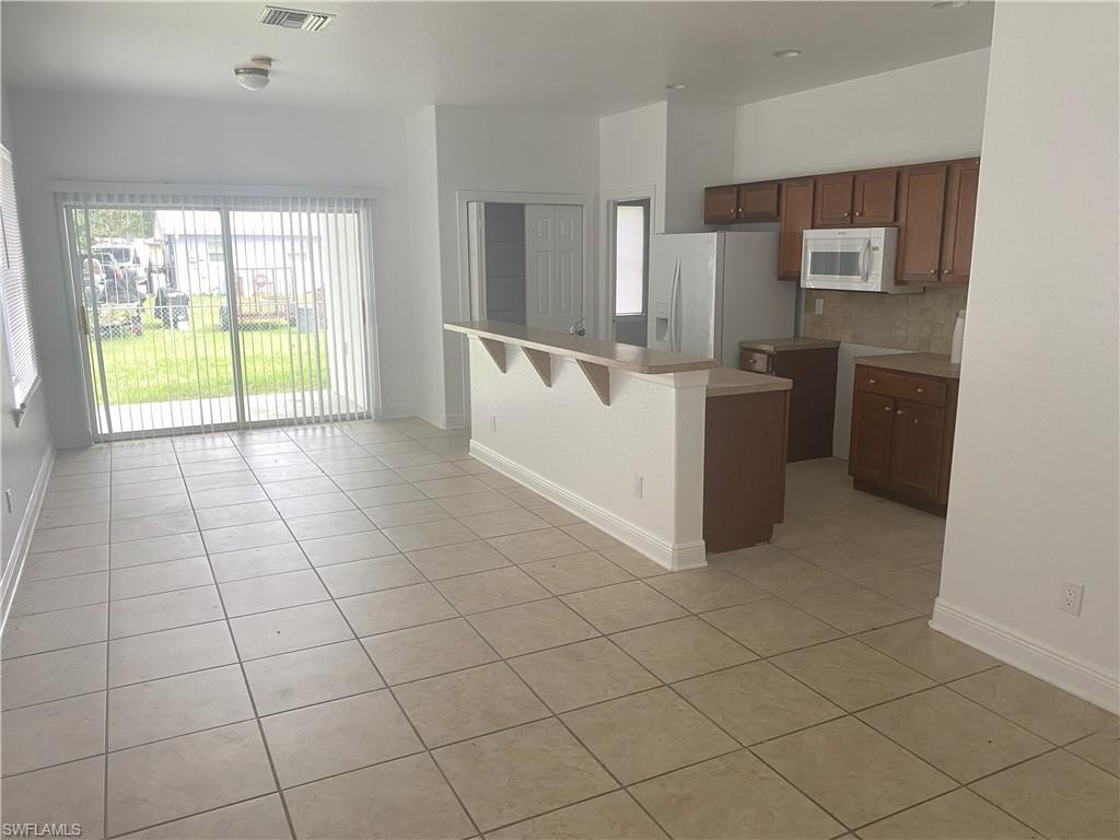 Kitchen and living area featuring tile flooring, sliding glass patio doors, a breakfast bar, wood cabinetry, and a built-in microwave