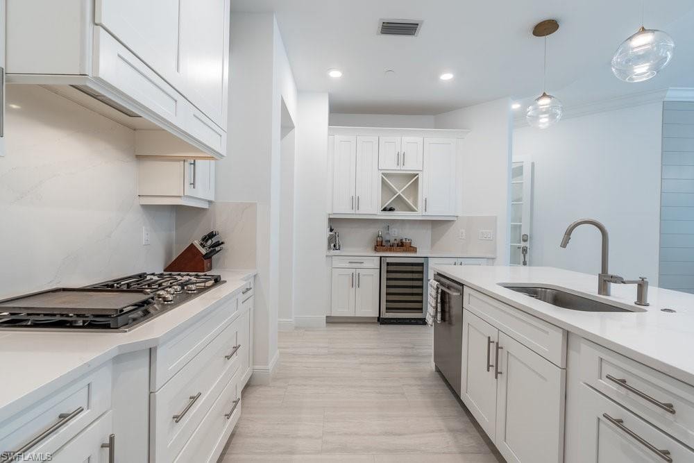 Kitchen featuring appliances with stainless steel finishes, white cabinets, beverage cooler, sink, and tasteful backsplash