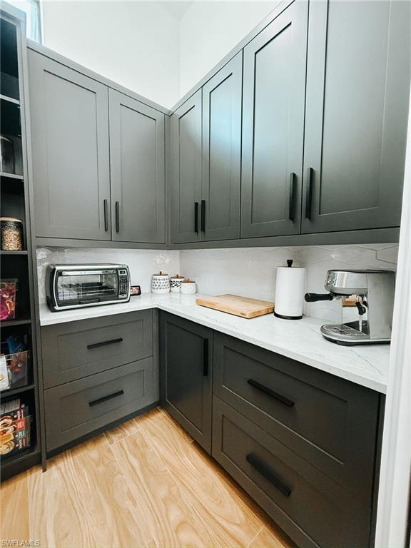 Corner pantry featuring charcoal-colored shaker cabinetry with black hardware, white stone countertops, and a white subway tile backsplash