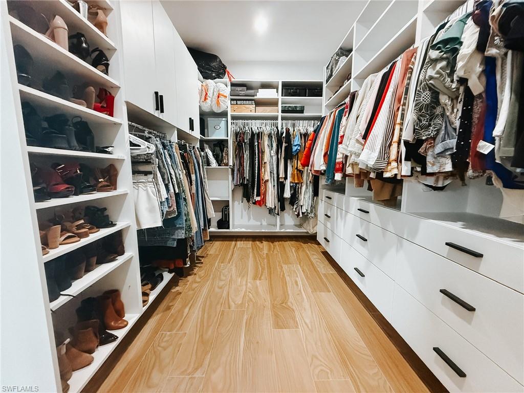 Custom closet with wood-finish flooring, white built-in shelving, integrated drawers with dark hardware, and ample hanging storage