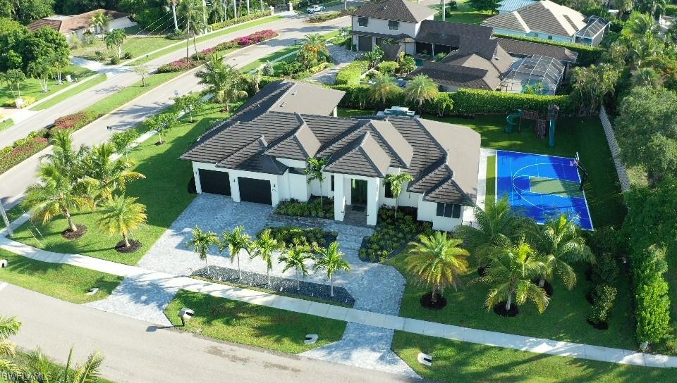 Modern single-story residence with a multi-car garage, extensive paver driveway, and a private sports court