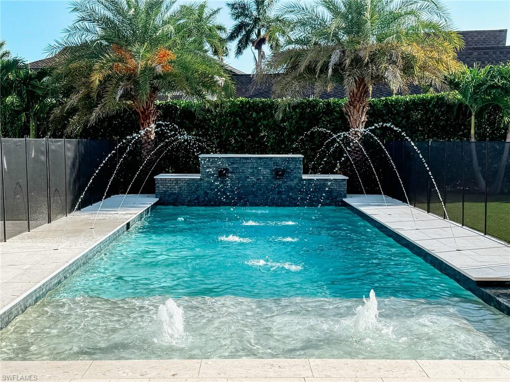 Rectangular swimming pool featuring a tiered stone-finish water feature, multiple water jets, and a baja shelf