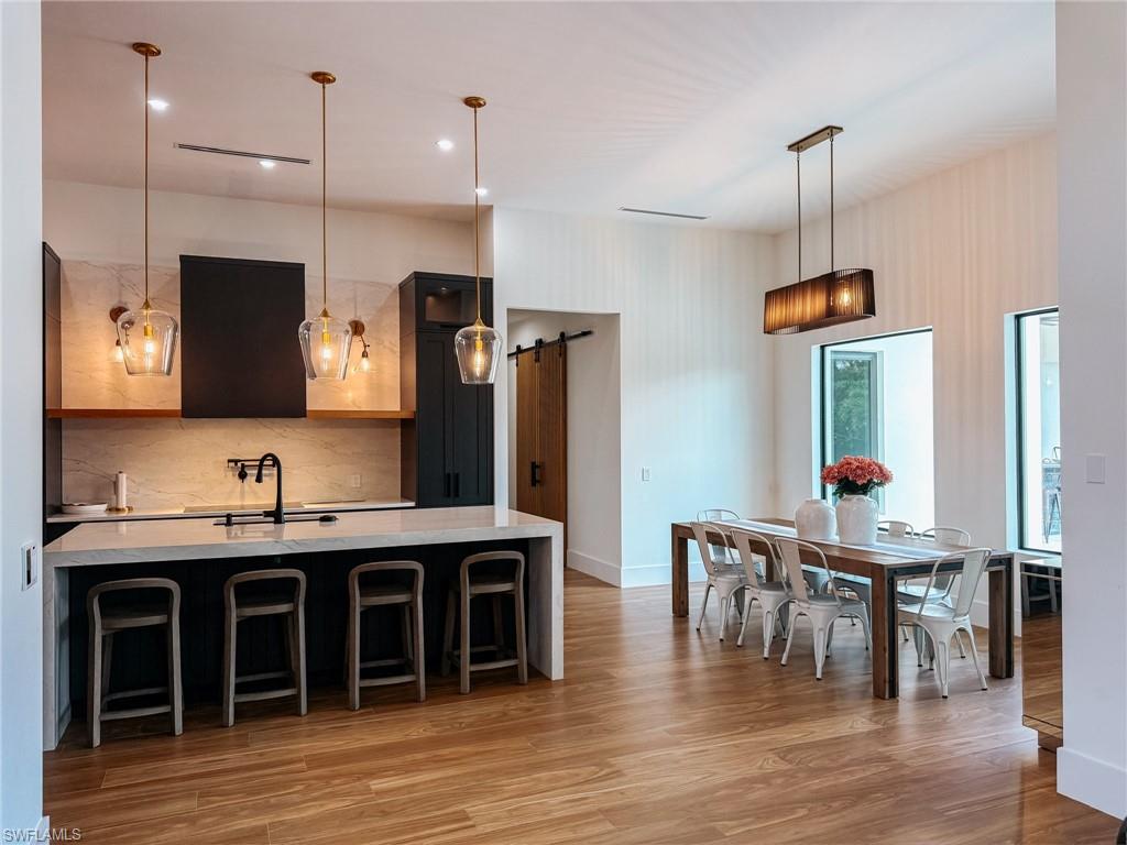 Open-concept kitchen and dining area featuring wood-finish flooring, a kitchen island with seating, dark cabinetry, and a light-toned backsplash