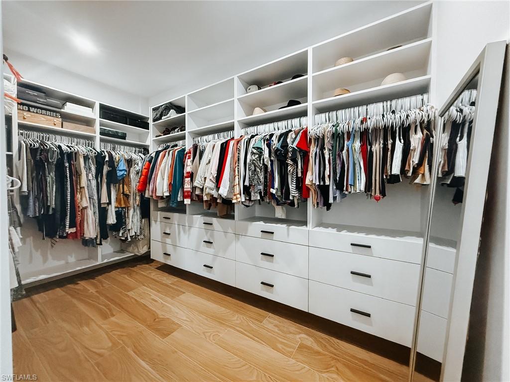 Custom walk-in closet featuring built-in white cabinetry, integrated hanging rods, open shelving, drawer storage with black hardware, and wood-finish flooring