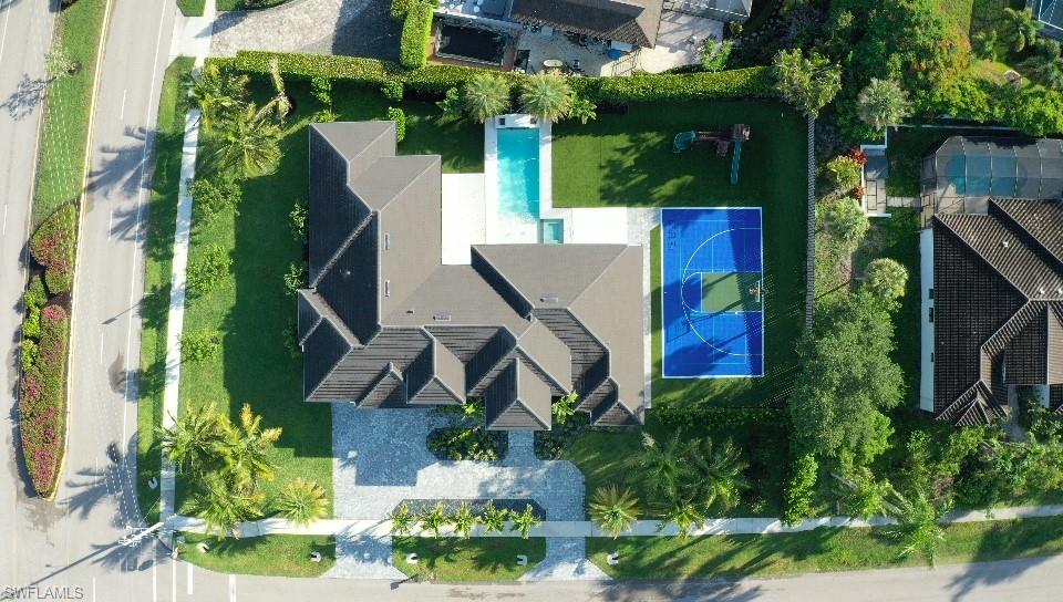 Expansive property featuring a multi-gabled roofline, a generously sized swimming pool, a full-sized basketball court, a lush lawn, and mature palm trees