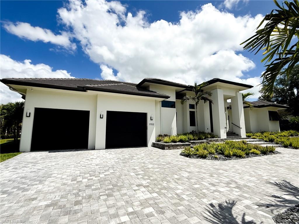 Contemporary residence featuring a paver driveway, two-car garage, and a covered entry with columns