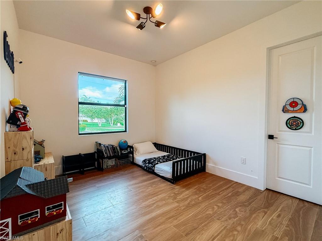 Bright room with wood-finish flooring, a contemporary ceiling light fixture, a single window, and a paneled white door with matte black hardware