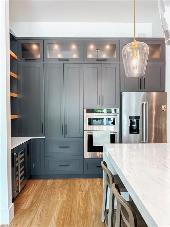 Contemporary kitchen featuring dark gray cabinetry, integrated stainless steel appliances, wood-finish flooring, and a large central island with a light-toned countertop