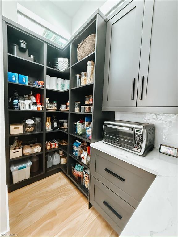 Walk-in pantry featuring extensive built-in shelving, light wood-finish flooring, and a transom window