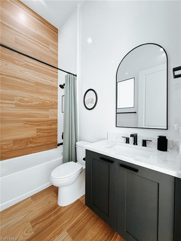 Bathroom featuring wood-finish tile flooring, a dark gray vanity with a white countertop and integrated sink, a contemporary arched mirror, and a shower with wood-finish wall tile
