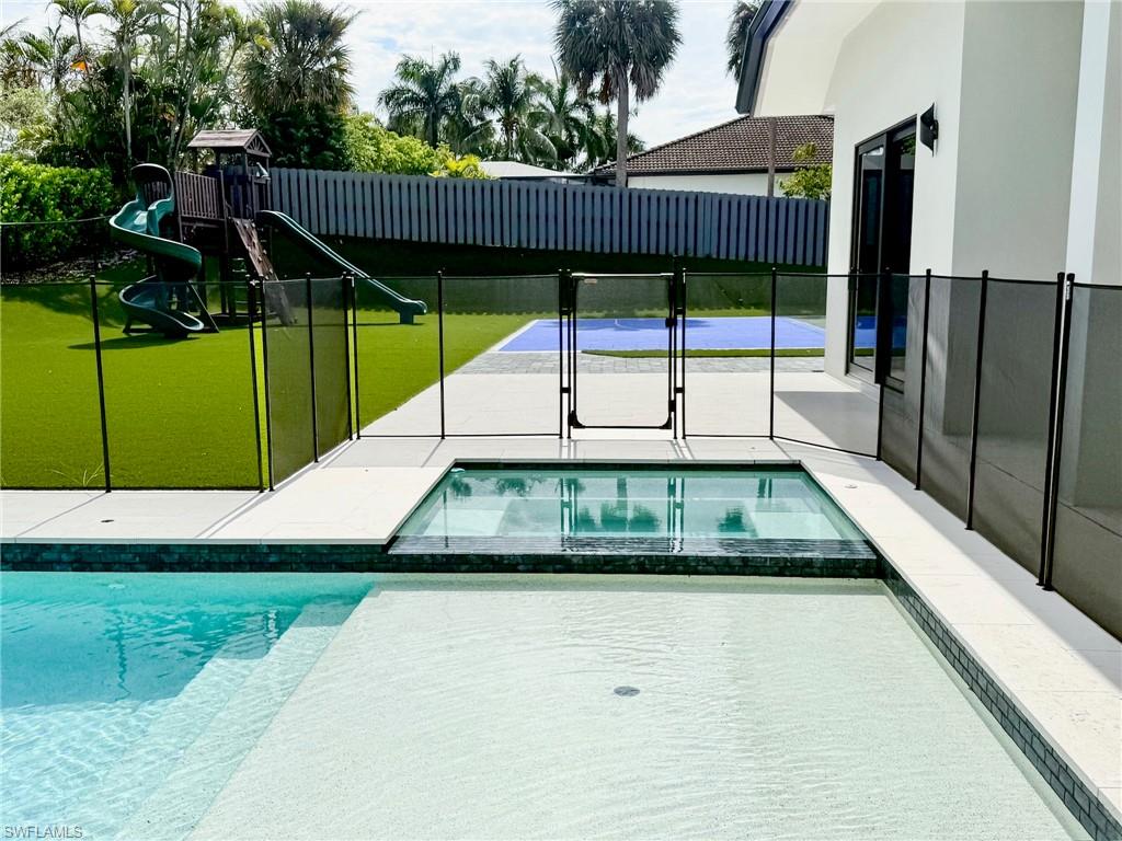 Outdoor living area featuring a swimming pool, integrated spa, and a turf-covered lawn