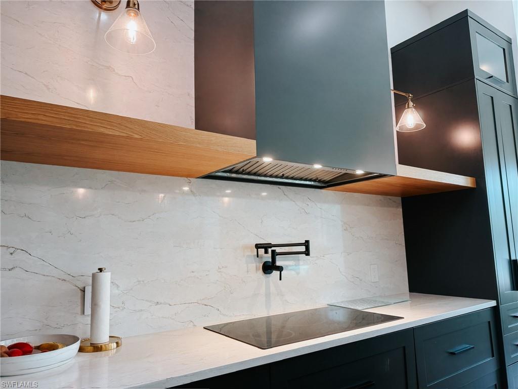 Modern kitchen featuring a slate grey range hood with integrated lighting, a matte black induction cooktop, and a matching wall-mounted pot filler