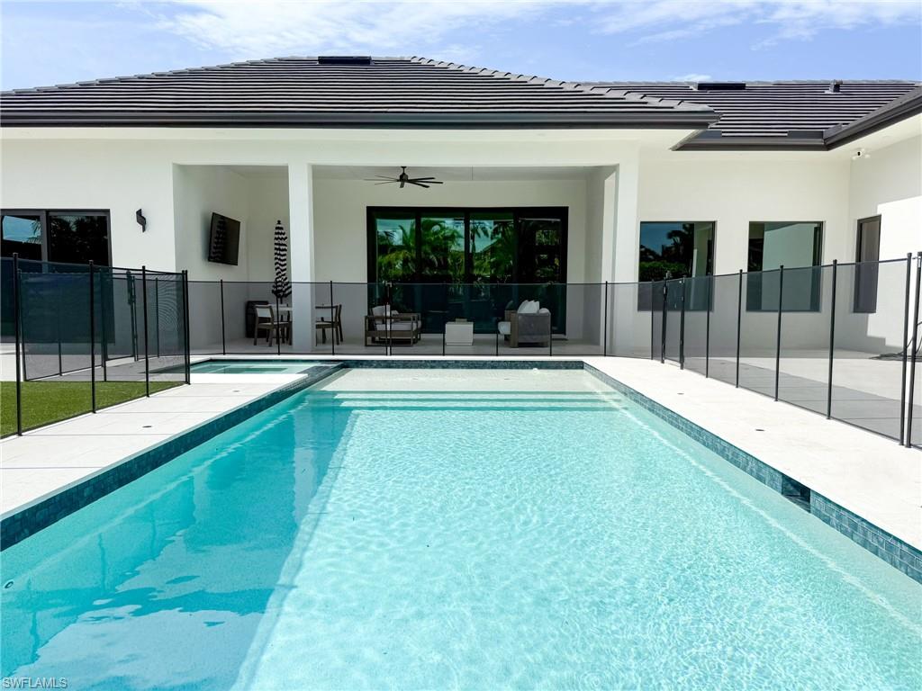 Contemporary home exterior featuring a rectangular pool with integrated spa, expansive white patio decking, a covered lanai with recessed lighting and a ceiling fan, and black-framed windows
