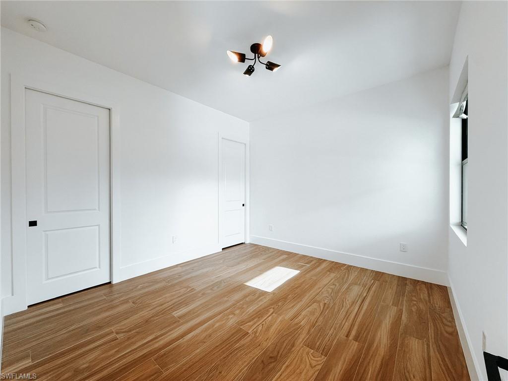 Bright interior featuring wood-finish flooring, two panel-style doors with matte black hardware, a multi-directional ceiling light fixture, and a window for natural illumination