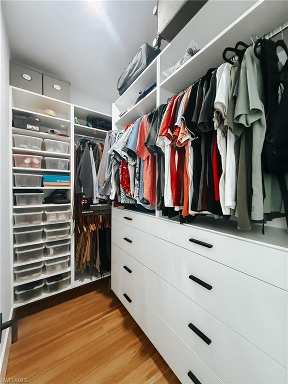 Custom closet system featuring white cabinetry, integrated shelving, hanging rods, and wood-finish flooring