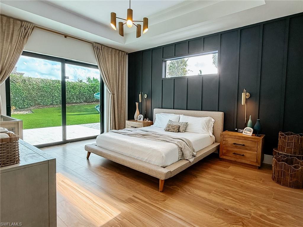 Spacious room featuring wood-finish flooring, a full-height sliding glass door leading to a green lawn, a dark accent wall with horizontal paneling, a horizontal window, and a modern chandelier