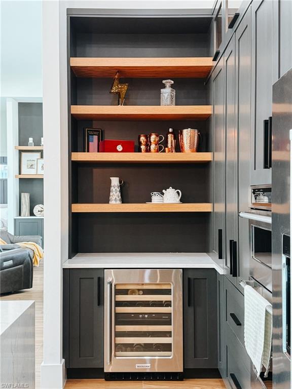 Built-in wine refrigerator with custom cabinetry, open wood shelving, light countertop, and wood-finish flooring
