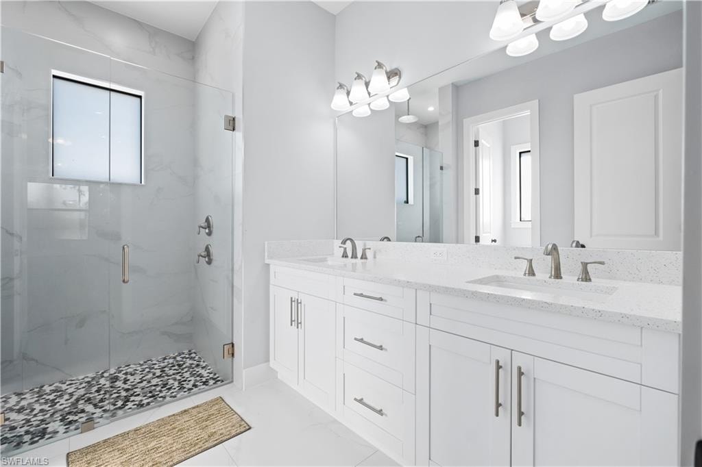 Spacious bathroom featuring a frameless glass shower enclosure, double vanity with integrated sinks, and stone-look countertops