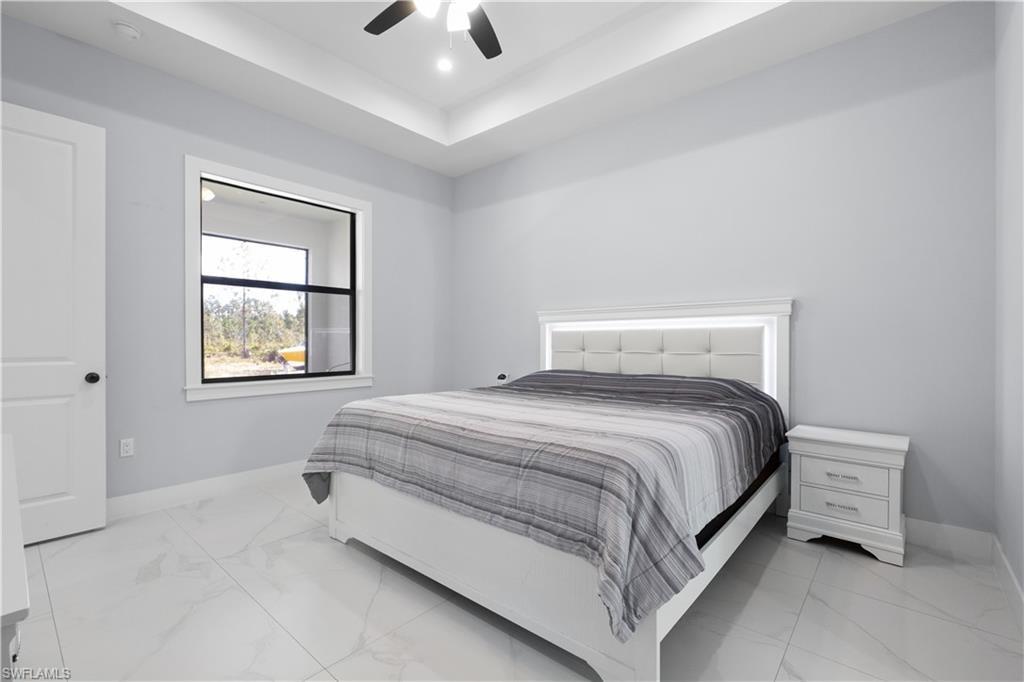 Spacious room featuring tray ceilings with recessed lighting, large format tile flooring, and a modern ceiling fan