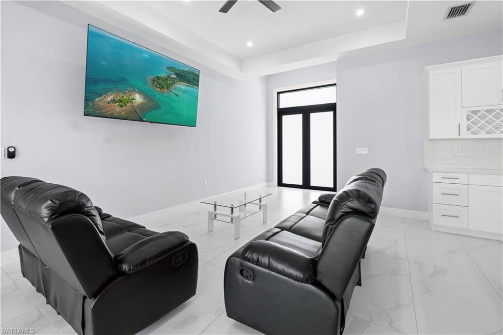 Spacious common area featuring light-toned tile flooring, a built-in wet bar with white cabinetry and a wine rack, and a ceiling fan