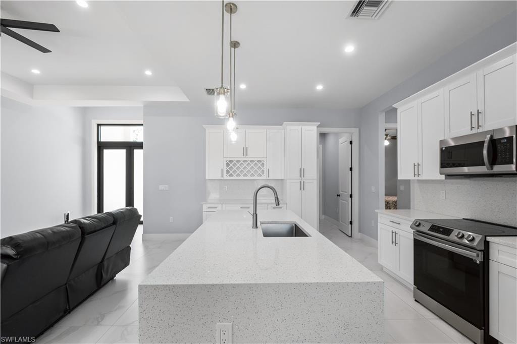 Open-concept kitchen featuring a large island with an undermount sink, pendant lighting, white cabinetry, stainless steel appliances, and tile flooring