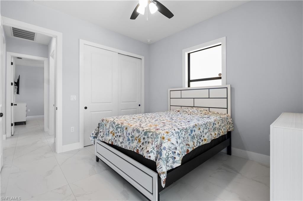 Well-lit room featuring tile flooring, a window with black trim, a ceiling fan, and white sliding closet doors