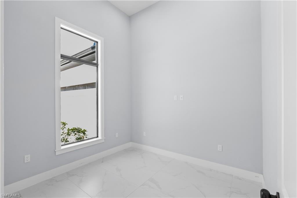 Room featuring a tall vertical window with white trim, light gray painted walls, and large format white tile flooring