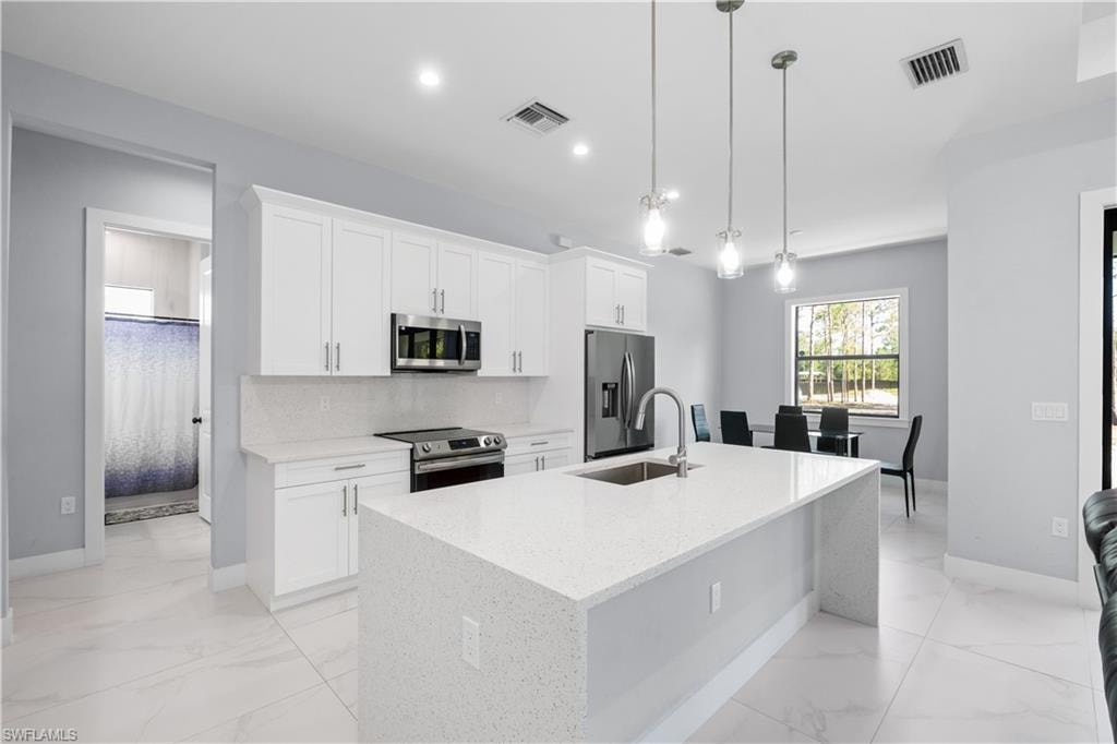 Open-concept kitchen featuring an expansive island with an undermount sink, white shaker cabinetry, stainless steel appliances, and large format white tile flooring