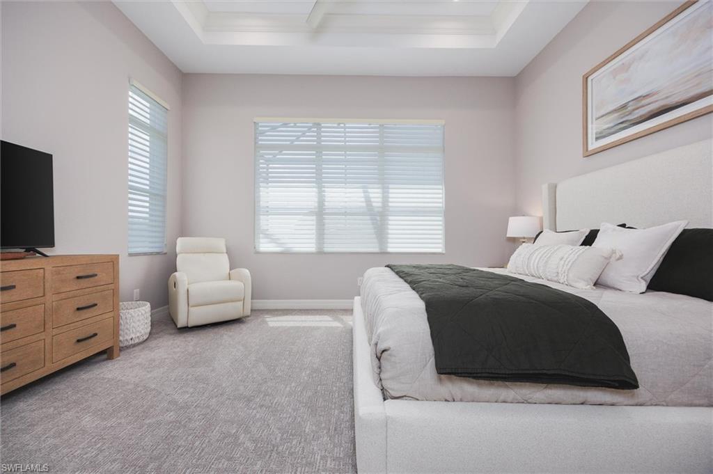 Bedroom featuring light-toned walls, tray ceiling, and dual windows with horizontal blinds