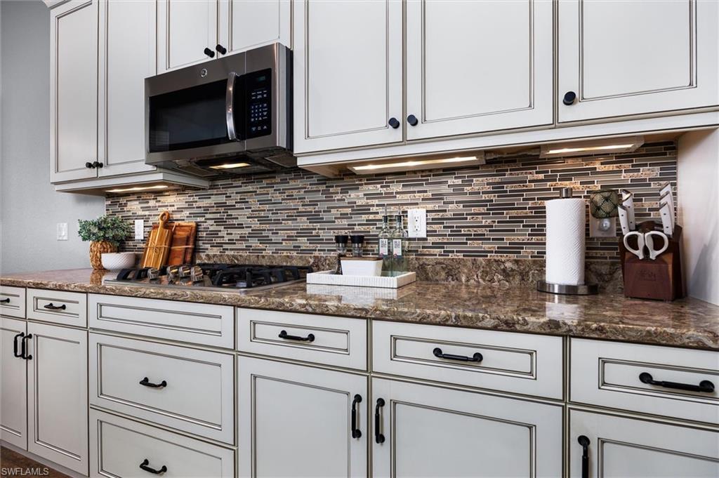 Kitchen featuring light-toned cabinetry with dark hardware, a built-in stainless steel microwave, a gas cooktop, under-cabinet lighting, and a mosaic tile backsplash