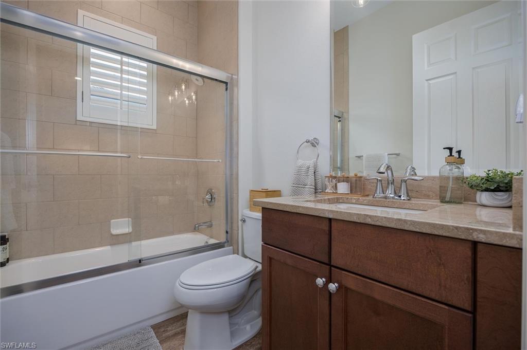 Bathroom featuring a tub and shower combination with glass enclosure, beige wall tiling, and a window with plantation shutters