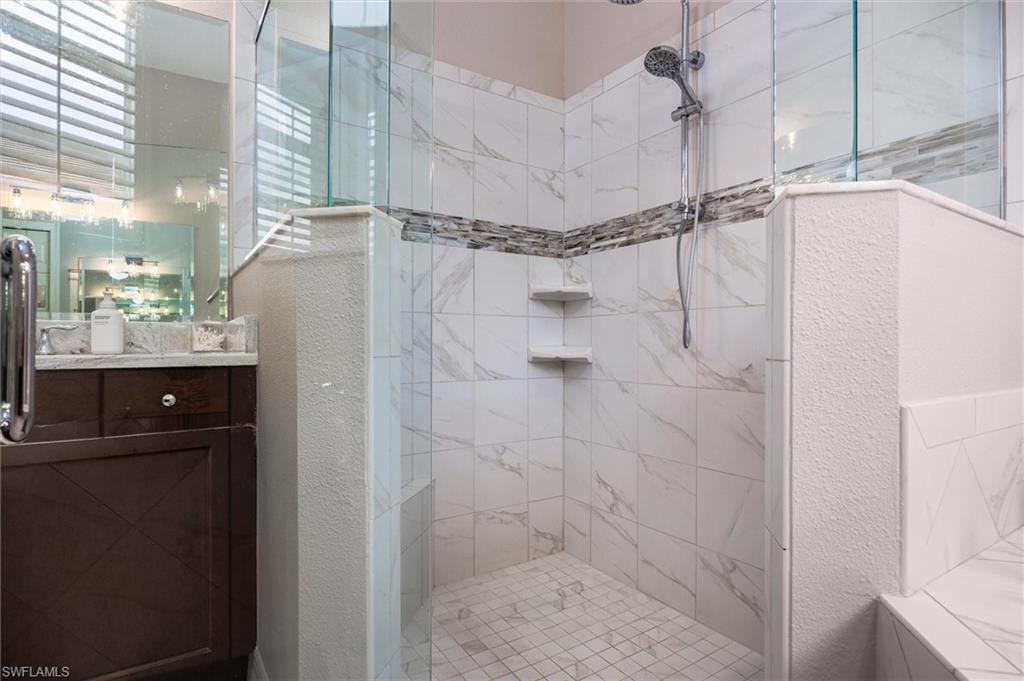 Walk-in shower featuring glass enclosure, handheld shower fixture, built-in shelving, white tile with subtle veining, and a decorative tile accent band