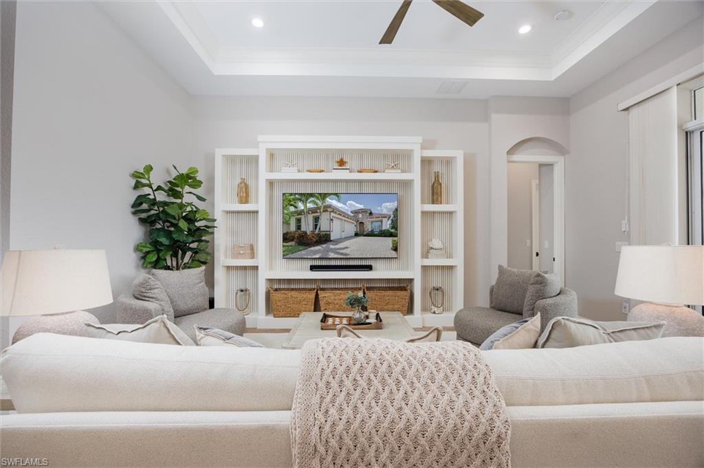 Living area featuring a tray ceiling with a ceiling fan, recessed lighting, and a built-in entertainment center with open shelving and storage baskets