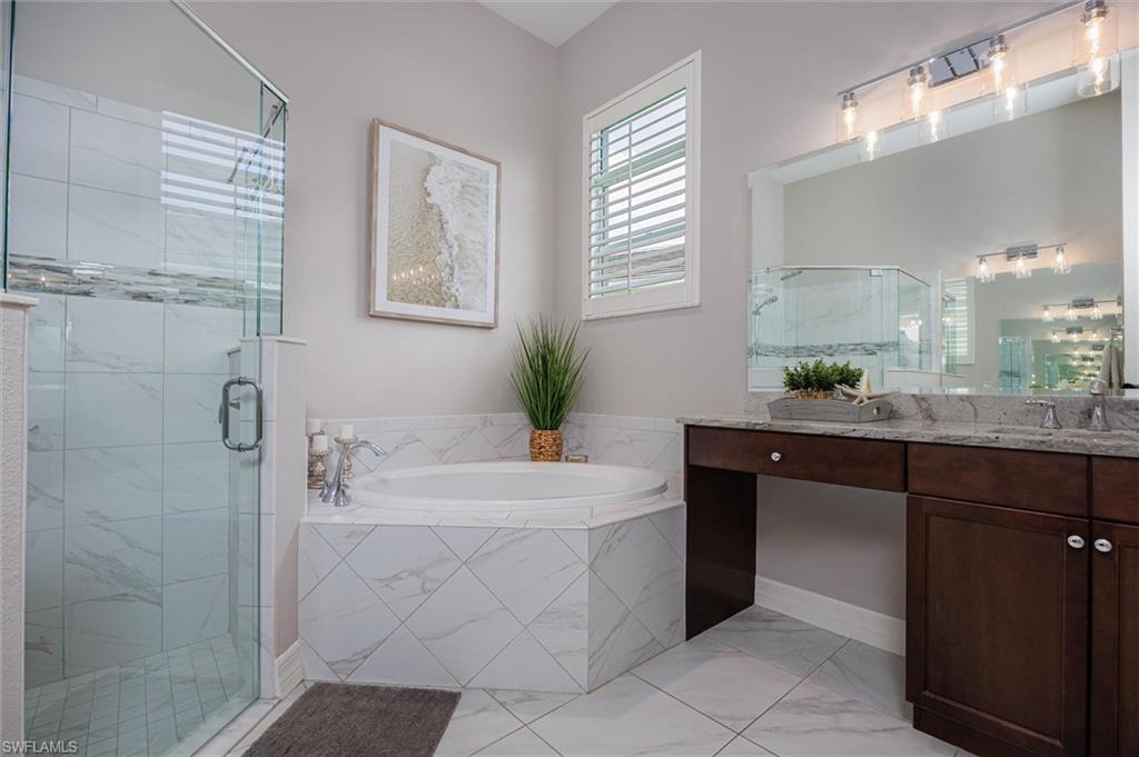Spacious bathroom featuring a glass-enclosed shower with subway tile, a built-in garden tub with a tiled surround, a double vanity with a stone countertop, an integrated makeup vanity, and a large mirror with overhead lighting