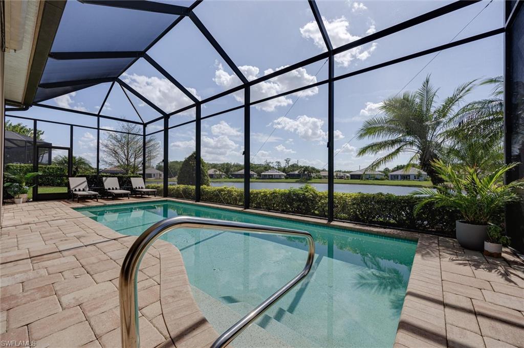 Screened outdoor swimming pool area featuring a paver deck, stainless steel grab rail, and waterfront setting