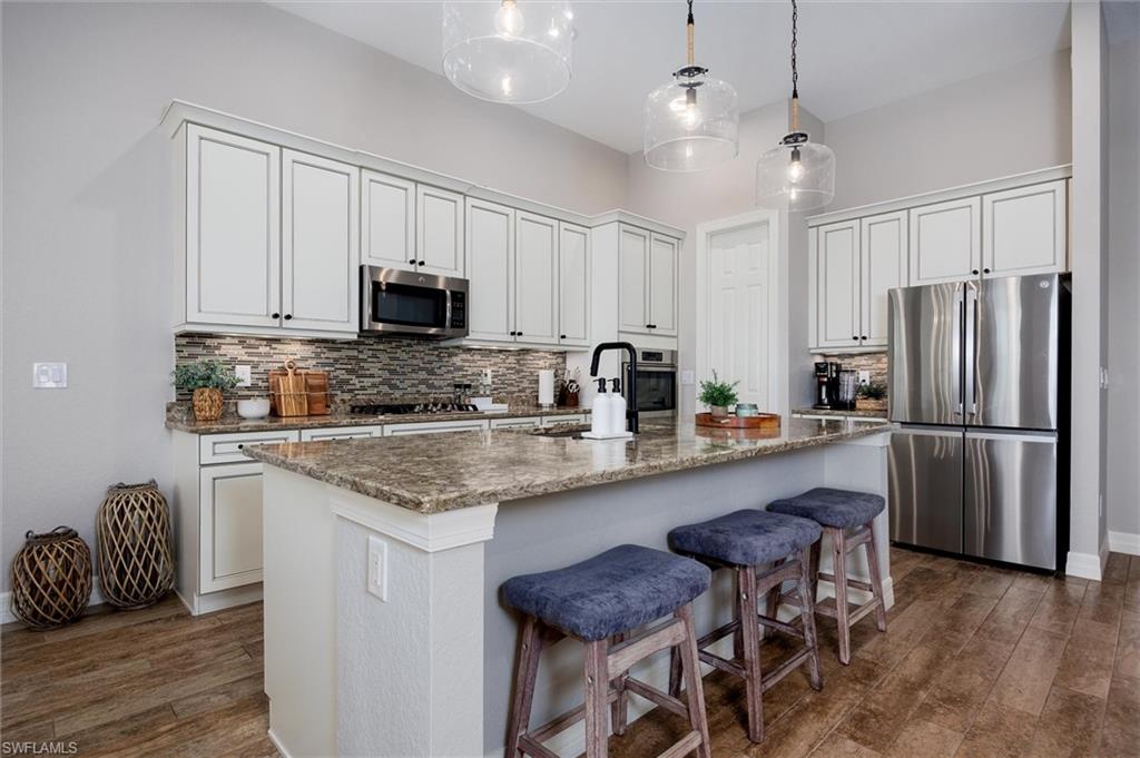 Kitchen featuring an expansive island with a granite-style countertop, white cabinetry with dark hardware, stainless steel appliances, a multi-tone tile backsplash, and wood-finish flooring