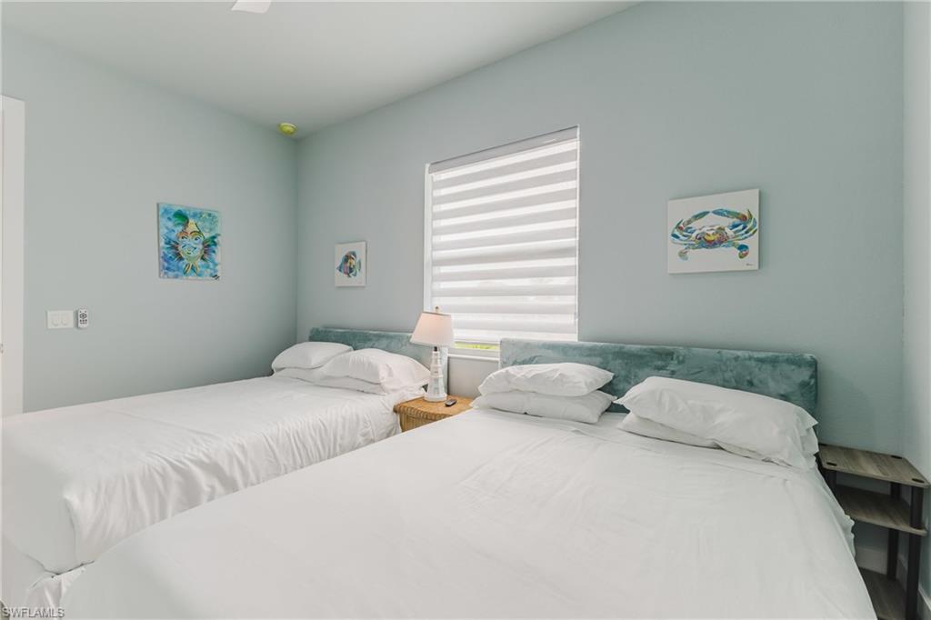 Bedroom featuring light blue walls, a window with horizontal blinds, a white ceiling fan, and two beds with upholstered headboards
