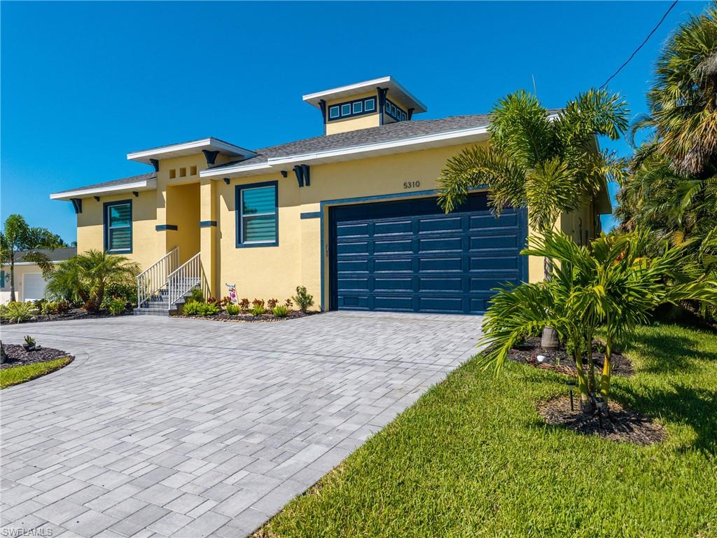 Contemporary exterior with a prominent paver driveway, an integrated two-car garage, and mature palm landscaping