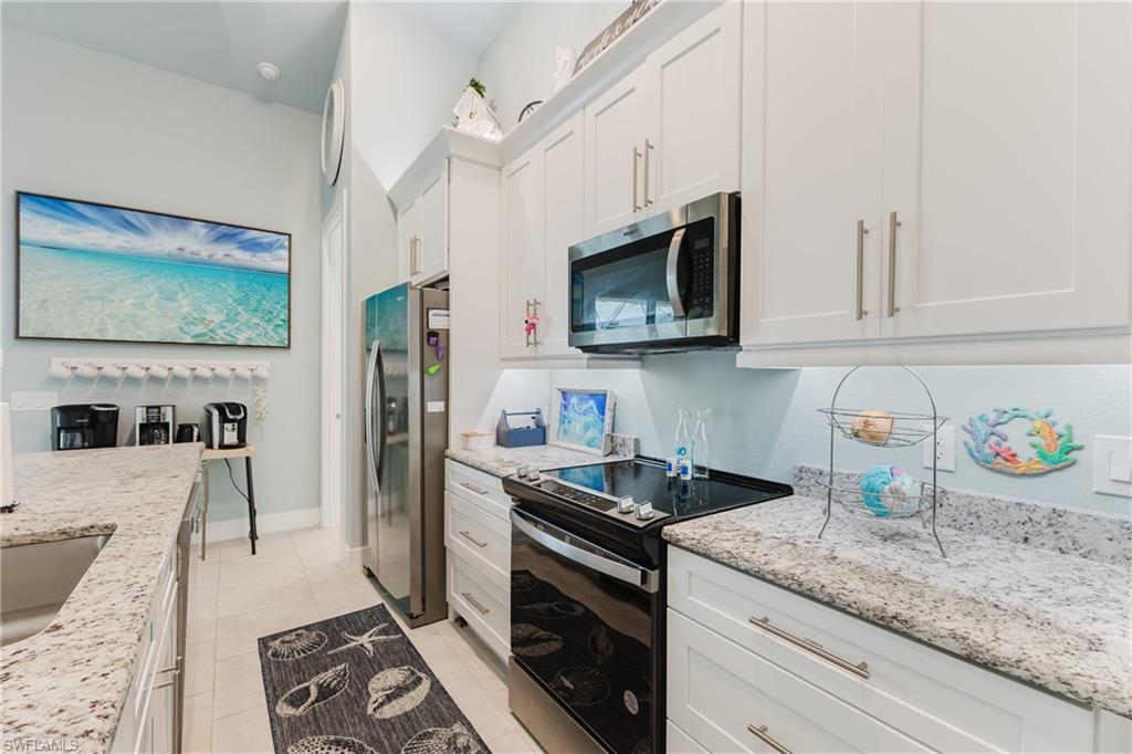 Galley kitchen featuring white shaker cabinetry, speckled countertops, stainless steel appliances, and tile flooring